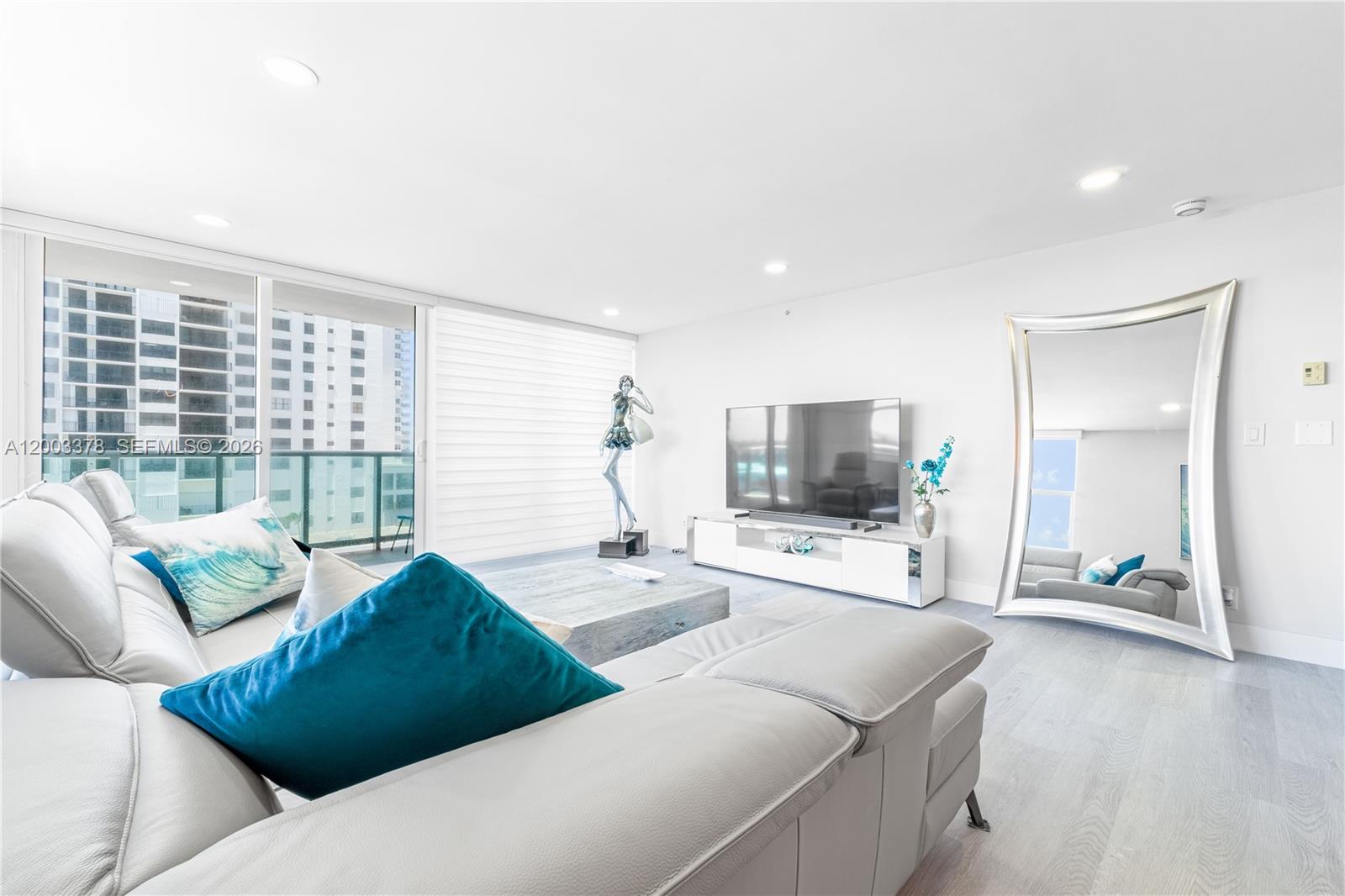 A modern living room features a grey sectional sofa, a large television, and a floor mirror — 2501 S Ocean Dr # 536, Hollywood FL 33019, HOLLYWOOD, FL