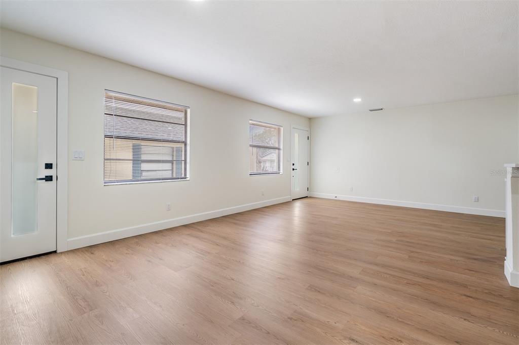 An empty room with light wood-look flooring, white walls, and two exterior doors — 8317 N MARKS STREET, TAMPA, FL