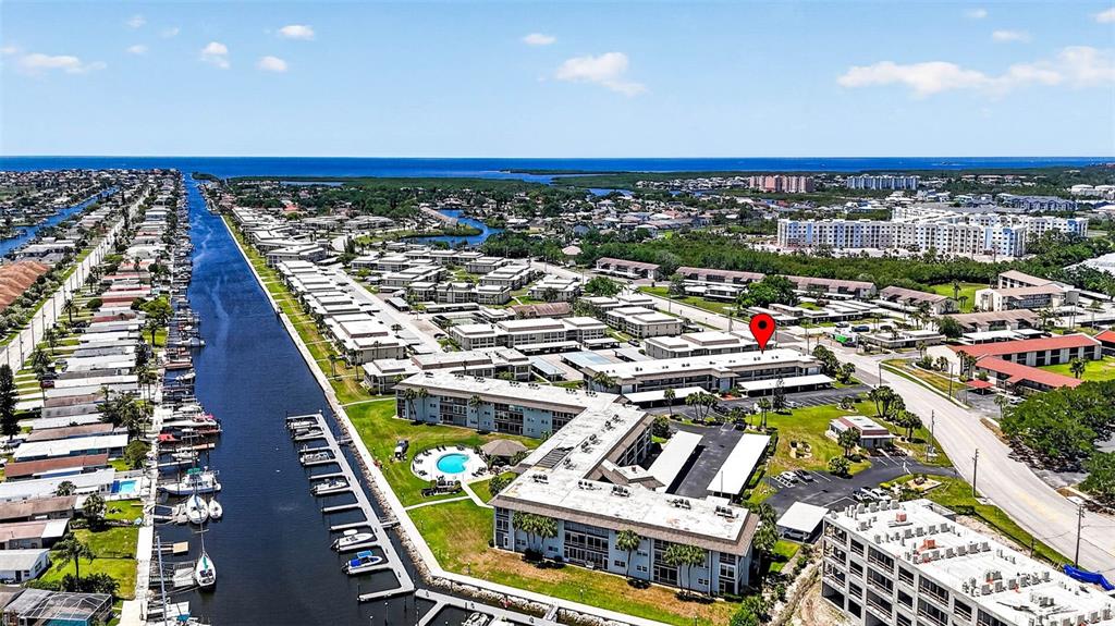 An aerial view shows a waterfront apartment complex with a canal, boats, and parking lots — 5197 SILENT LOOP UNIT 124, NEW PORT RICHEY, FL