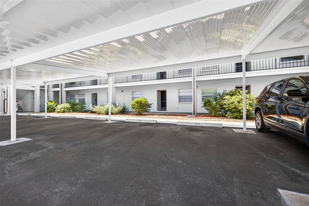 A covered parking area with numbered concrete wheel stops sits in front of an apartment building — 5197 SILENT LOOP UNIT 124, NEW PORT RICHEY, FL