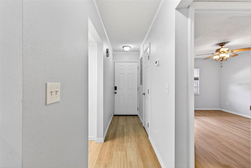 A hallway with light wood-look flooring leads to a white front door — 5197 SILENT LOOP UNIT 124, NEW PORT RICHEY, FL