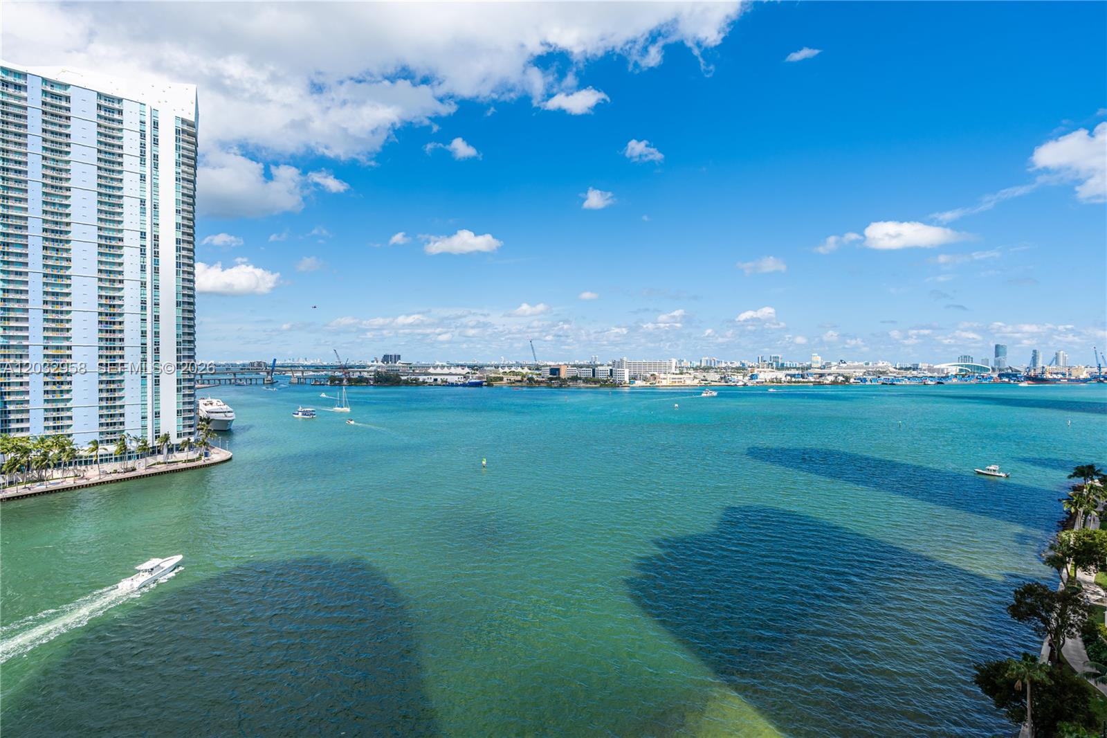 A tall residential building stands beside a wide bay with boats under a blue sky — 900 Brickell Key Blvd # 1002, Miami FL 33131, MIAMI, FL
