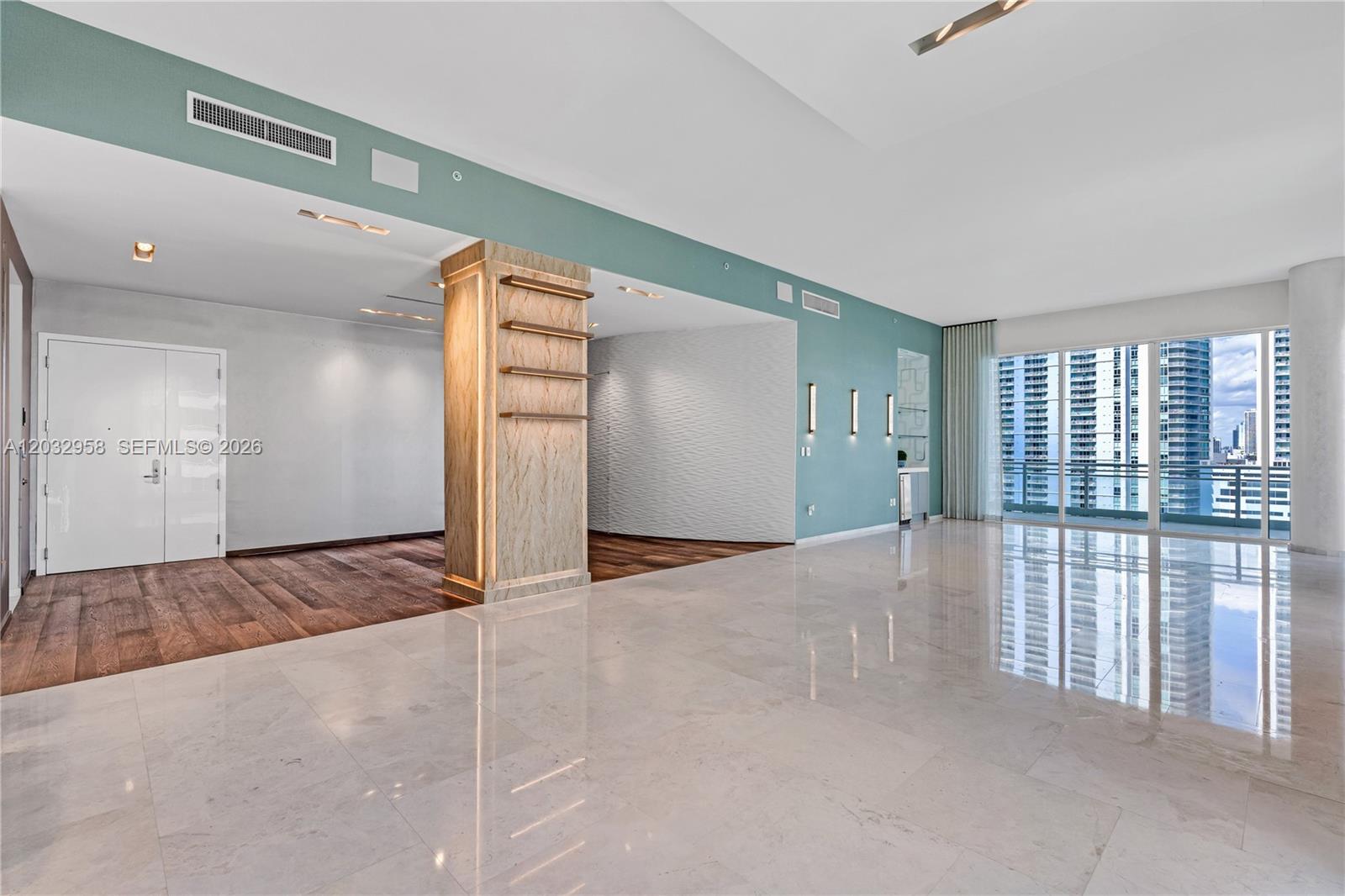 A spacious room features marble flooring, a wood-paneled column, and a teal accent wall — 900 Brickell Key Blvd # 1002, Miami FL 33131, MIAMI, FL