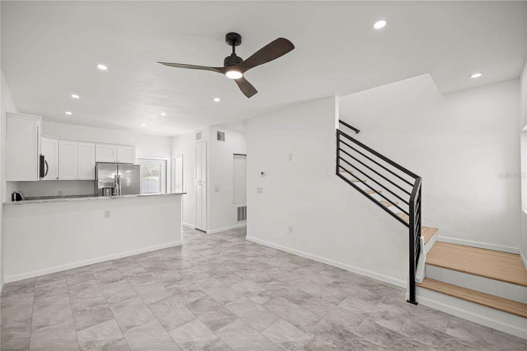 A kitchen with white cabinets and a staircase with a black railing in an open-concept room — 305 SE 5TH TERRACE, WILLISTON, FL