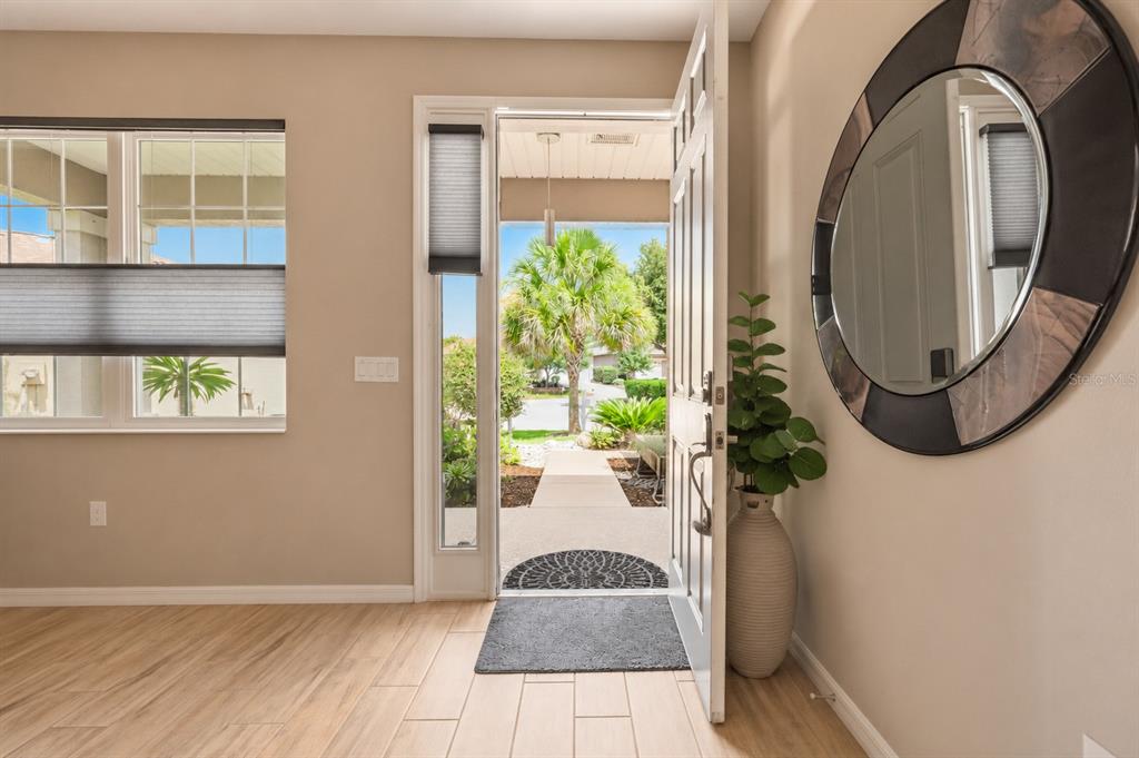 An entryway with light wood-look tile flooring, a circular mirror, and an open front door — 8221 SW 78TH TERRACE ROAD, OCALA, FL