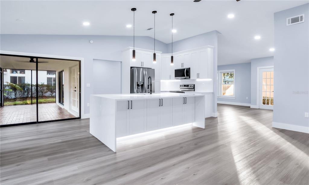 A modern kitchen features white cabinetry, a large island with under-cabinet lighting, and wood-look flooring — 1007 NW 82ND STREET, BRADENTON, FL