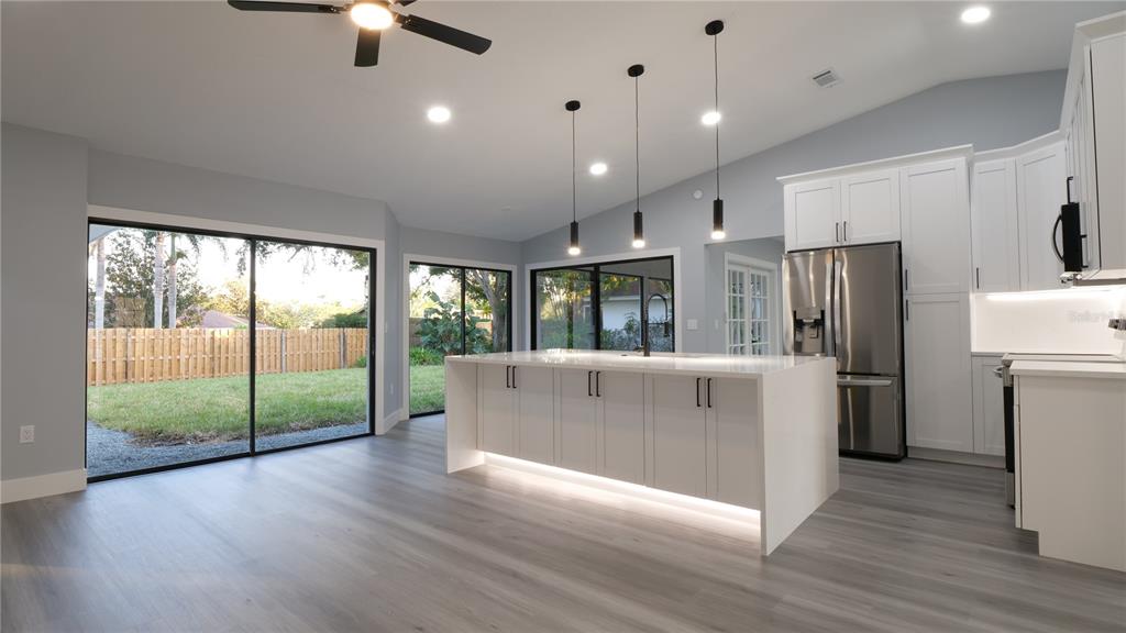 A modern kitchen features a white island with under-cabinet lighting, stainless appliances, and sliding doors — 1007 NW 82ND STREET, BRADENTON, FL
