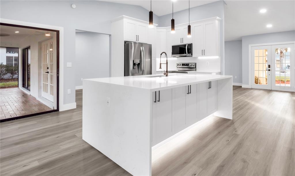 A modern kitchen features a large white quartz island, white cabinetry, and light wood flooring — 1007 NW 82ND STREET, BRADENTON, FL