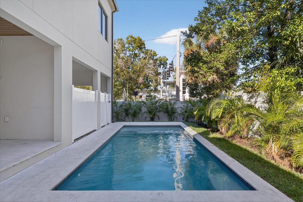 A rectangular swimming pool sits on a stone patio beside a modern white house — 3702 S LYNWOOD AVENUE, TAMPA, FL