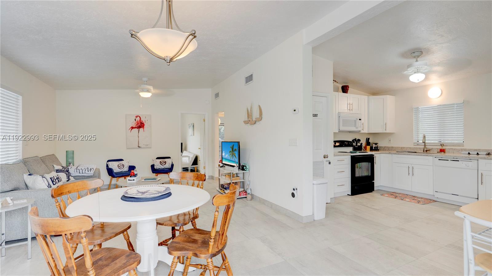An open-concept living and dining area features a white kitchen, tile floors, and wooden chairs — 137 Pacific Ave, Tavernier FL 33070, TAVERNIER, FL
