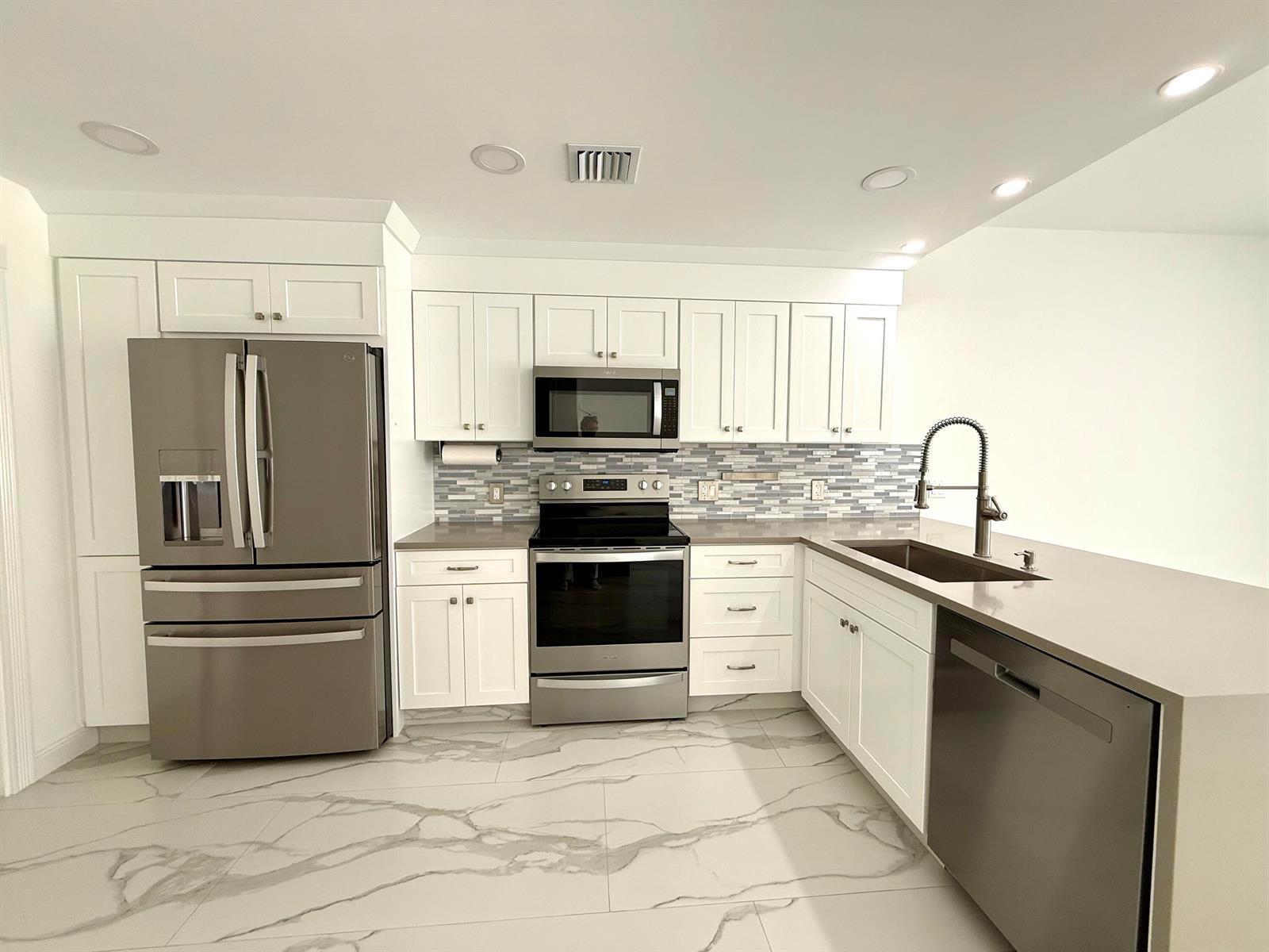 A modern kitchen features white cabinets, stainless steel appliances, and gray marble-patterned tile flooring — 117 Waterford Drive, Jupiter FL 33458, JUPITER, FL
