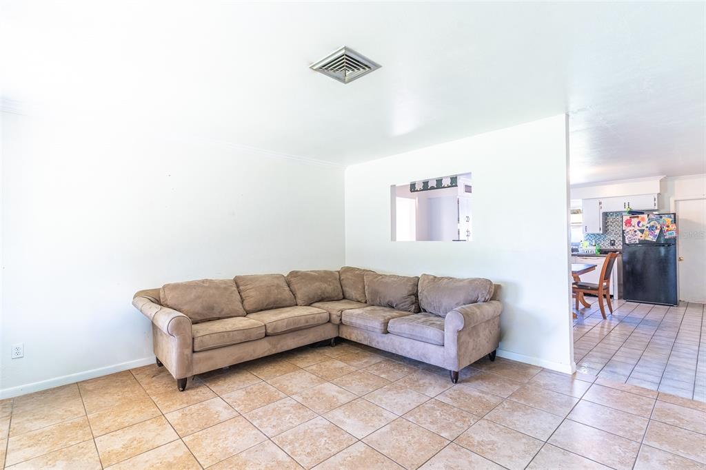 A living room with tan tile flooring, a large brown sectional sofa, and a pass-through window — 1500 AVENUE H NE, WINTER HAVEN, FL