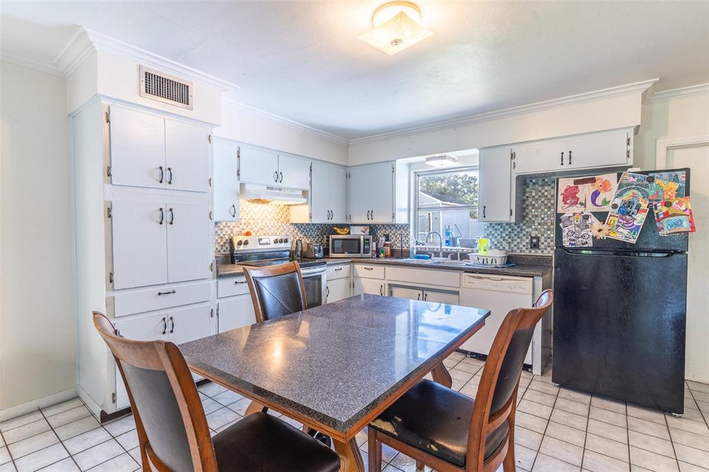 A kitchen with white cabinets, a dark dining table, and a black refrigerator — 1500 AVENUE H NE, WINTER HAVEN, FL