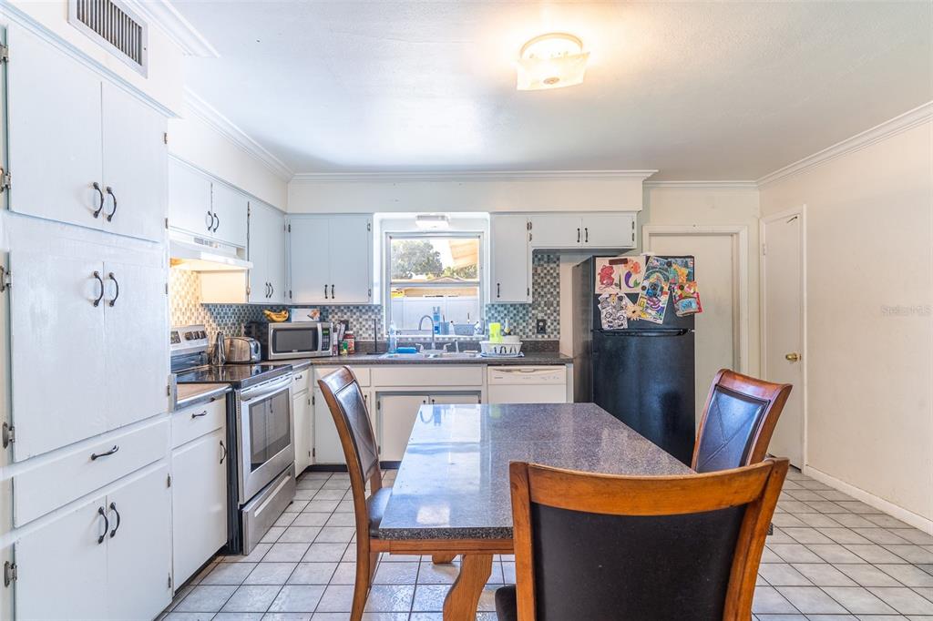 A kitchen features white cabinets, a black refrigerator, a dining table, and tiled flooring — 1500 AVENUE H NE, WINTER HAVEN, FL