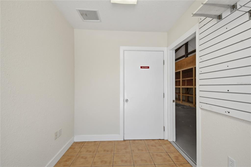 A tiled room features a white restroom door and a wall-mounted slatwall display panel — 200 WALER WAY UNIT G&H, ST AUGUSTINE, FL