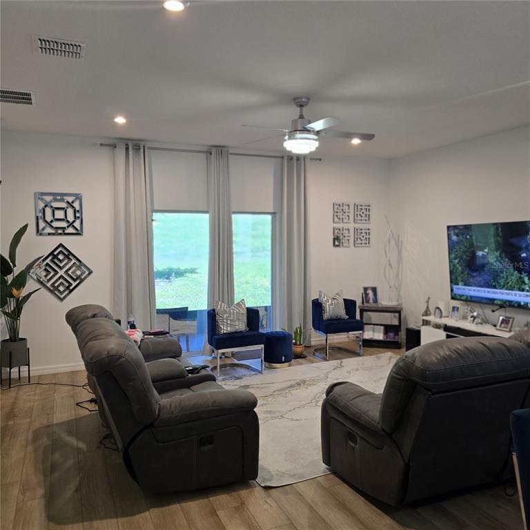 A living room features gray reclining sofas, blue accent chairs, and a large television — 33259 COUNTRY HOUSE DRIVE, SORRENTO, FL