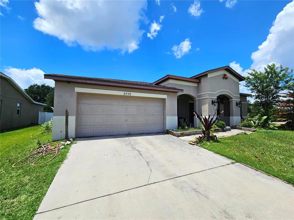 A single-story house with a beige stucco exterior, a two-car garage, and a concrete driveway — 2750 CORBEL LOOP, KISSIMMEE, FL