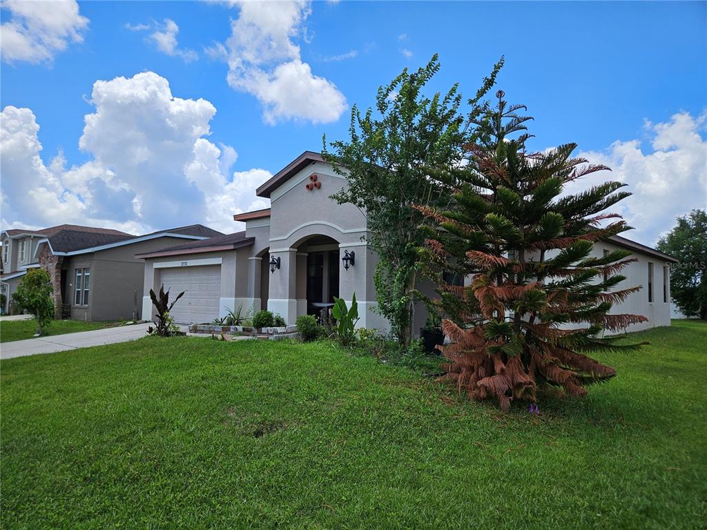 A single-story house with a tan stucco exterior, a two-car garage, and a front lawn — 2750 CORBEL LOOP, KISSIMMEE, FL