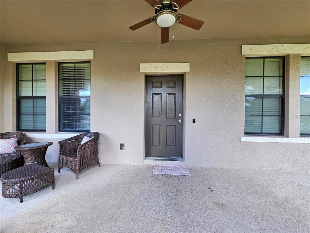 A covered patio features a dark door, wicker furniture, and a ceiling fan — 2750 CORBEL LOOP, KISSIMMEE, FL