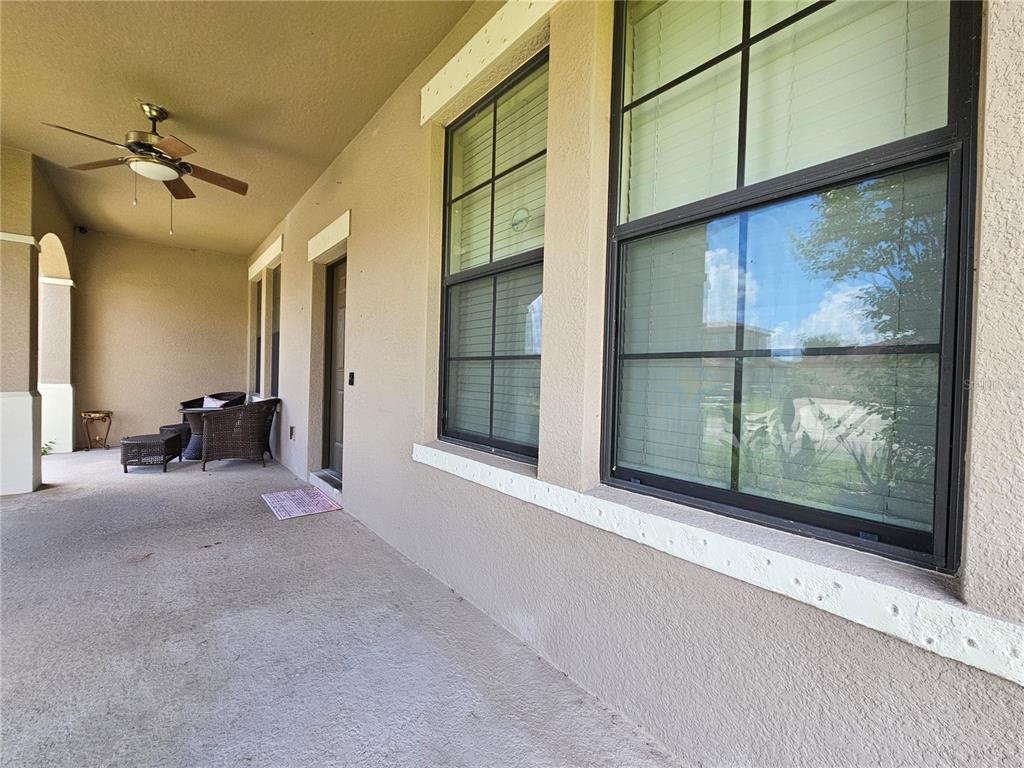 A covered patio features a ceiling fan, stucco walls, and large windows with dark frames — 2750 CORBEL LOOP, KISSIMMEE, FL