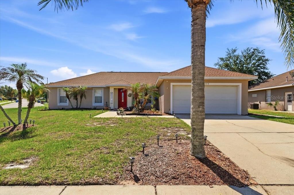 A single-story suburban house with a red front door, two-car garage, and palm trees — 4378 DINNER LAKE BOULEVARD, LAKE WALES, FL