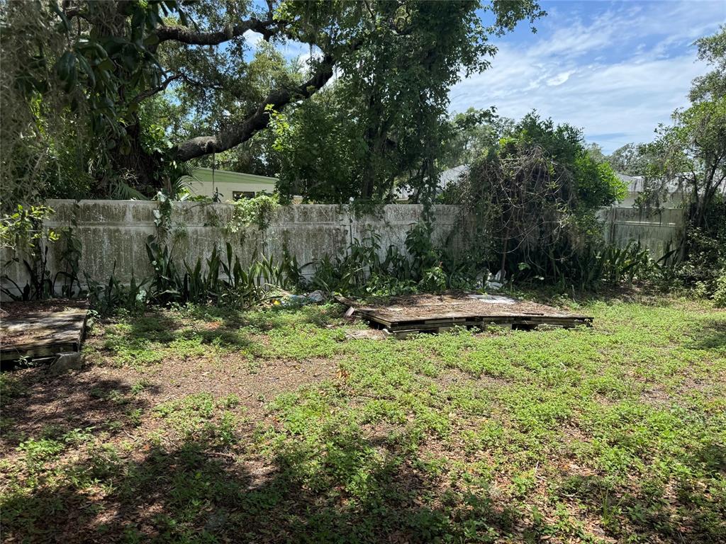A backyard features a weathered white fence, overgrown vegetation, and two wooden pallets on grass — 2609 E EMMA STREET, TAMPA, FL