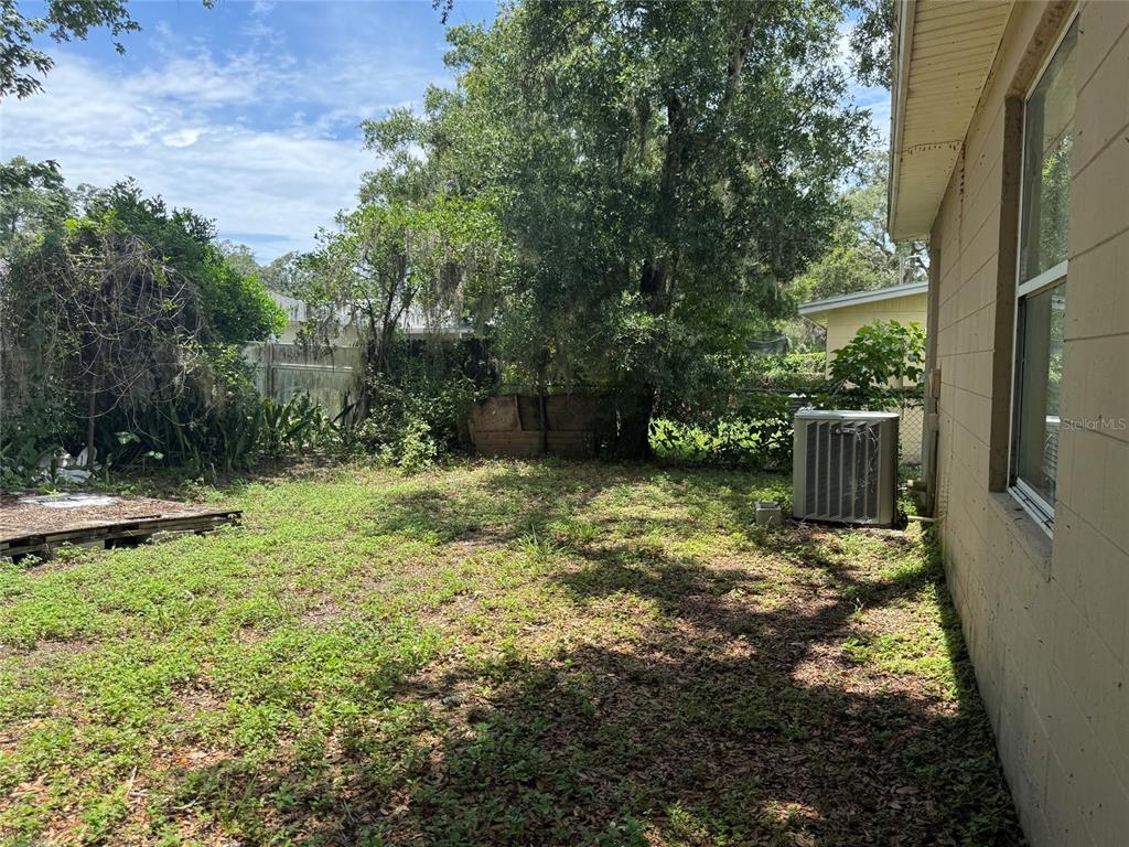 A grassy backyard features a large tree, an air conditioning unit, and a wooden pallet — 2609 E EMMA STREET, TAMPA, FL