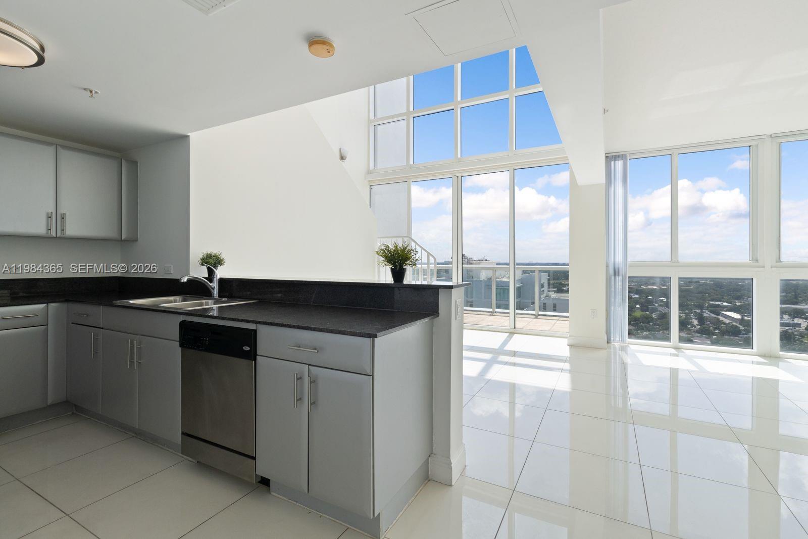 A kitchen with grey cabinets and granite countertops overlooks a living area with floor-to-ceiling windows — 1861 NW North River Dr # 3, Miami FL 33125, MIAMI, FL