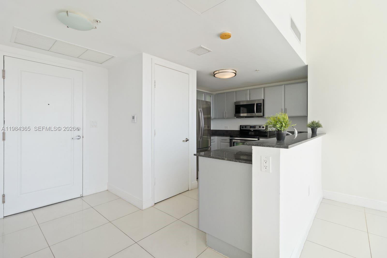 A kitchen with gray cabinets and granite countertops opens to a tiled entryway — 1861 NW North River Dr # 3, Miami FL 33125, MIAMI, FL