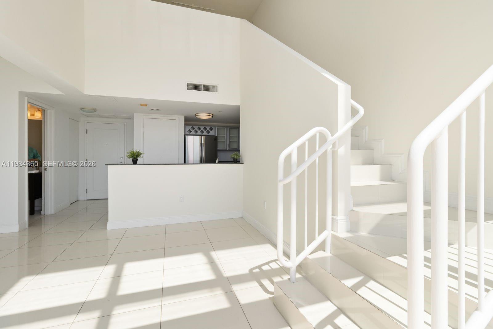 A bright, open-concept interior features white tile flooring, a staircase, and a kitchen area — 1861 NW North River Dr # 3, Miami FL 33125, MIAMI, FL