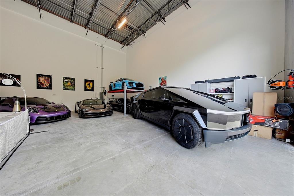 A high-ceilinged garage features a concrete floor, storage cabinets, and several luxury vehicles parked inside — 6500 MOTOR ENCLAVE WAY UNIT 814, TAMPA, FL