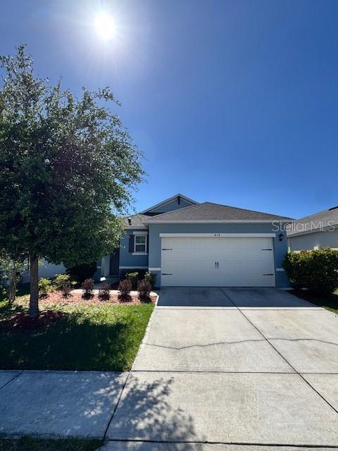 A single-story house with a white garage door and a tree in the front yard — 414 COOL SUMMER LANE, DAVENPORT, FL