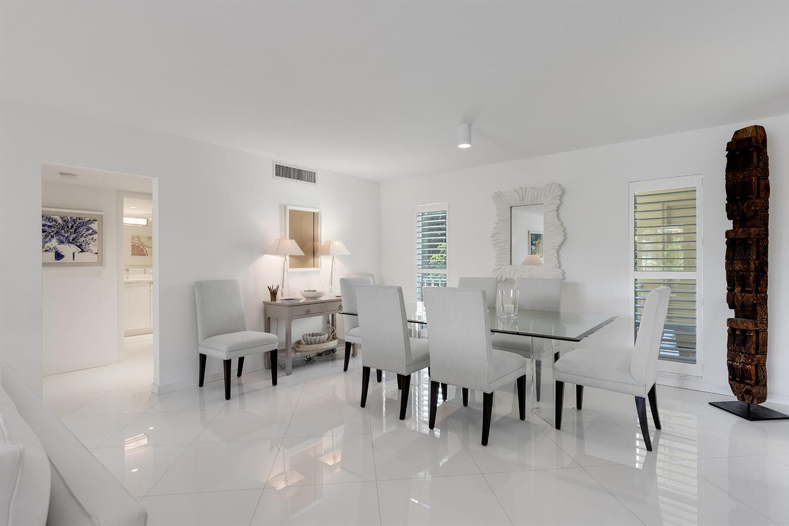 A bright dining room features white tile floors, a glass table, and a tall wooden sculpture — 227 Australian Avenue # 1e, Palm Beach FL 33480, PALM BEACH, FL
