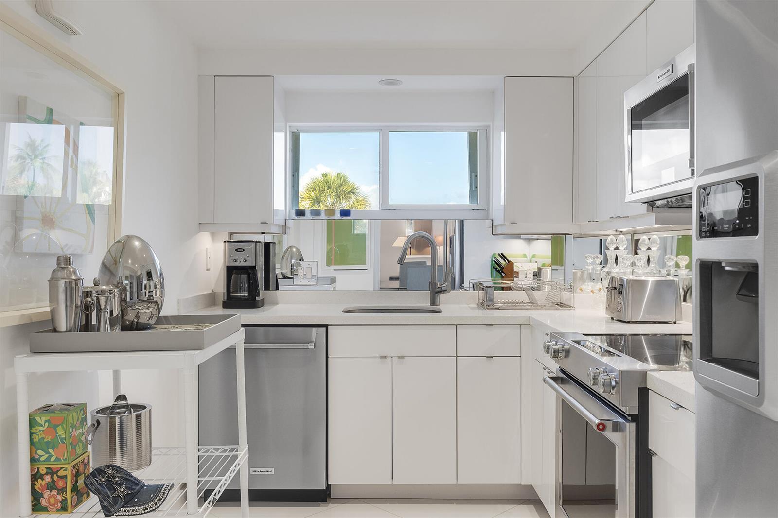 A modern white kitchen features stainless steel appliances, a window over the sink, and mirrored backsplash — 227 Australian Avenue # 1e, Palm Beach FL 33480, PALM BEACH, FL