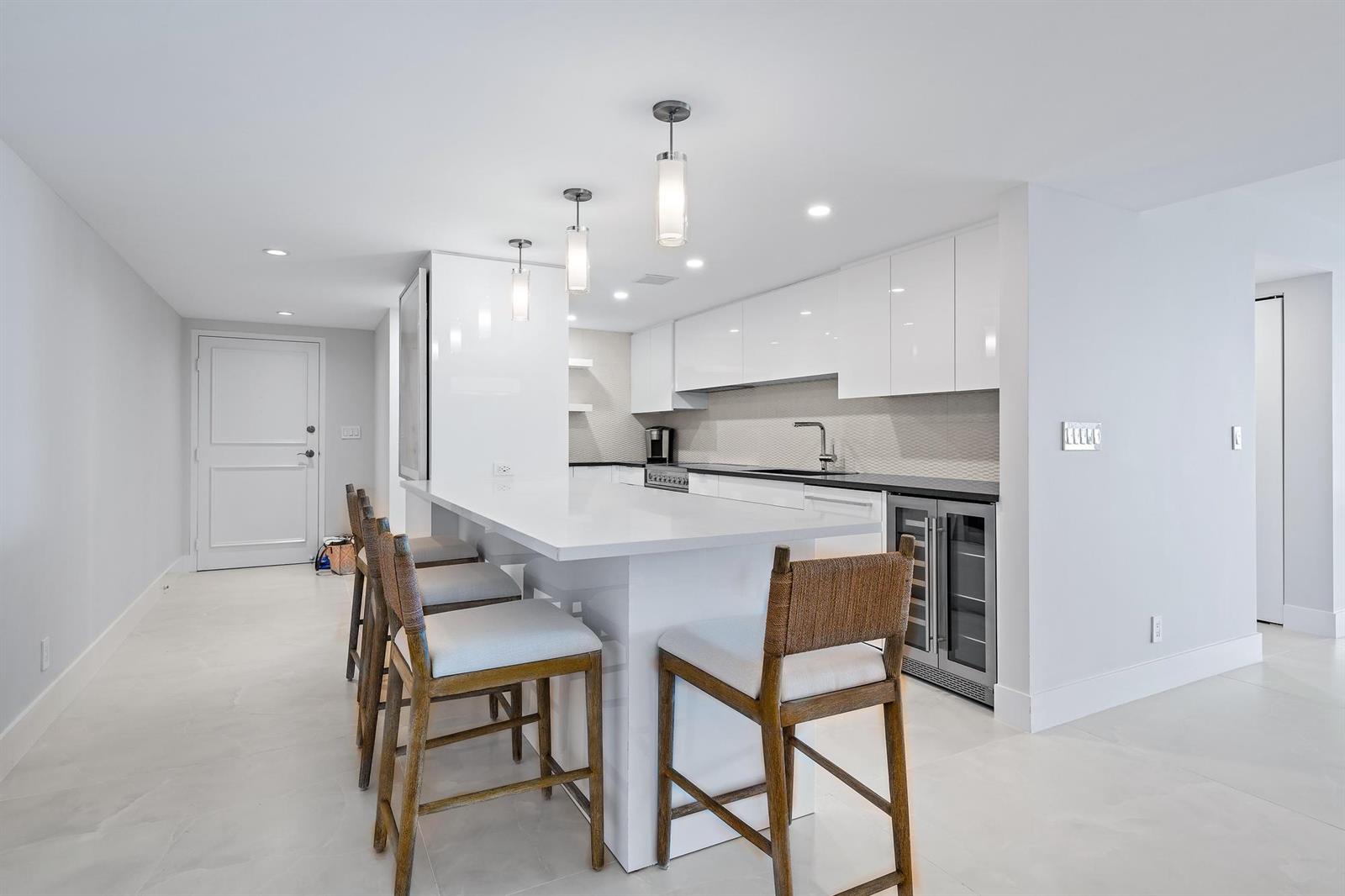 A modern kitchen features a white island with bar stools and glossy white cabinetry — 3456 S Ocean Boulevard # 701, Palm Beach FL 33480, PALM BEACH, FL