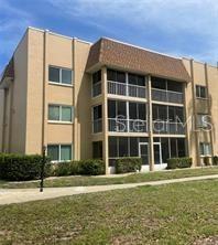 A three-story tan apartment building features screened-in balconies and a brown shingled roof — 1310 GLEN OAKS DRIVE E UNIT 385E, SARASOTA, FL