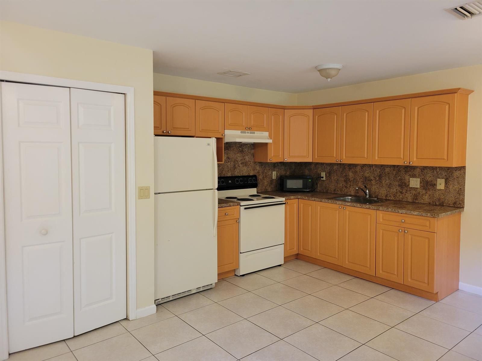 A kitchen features light wood cabinets, white appliances, a brown countertop, and beige tile flooring — 2227 Monroe Street # 2, Hollywood FL 33020, HOLLYWOOD, FL