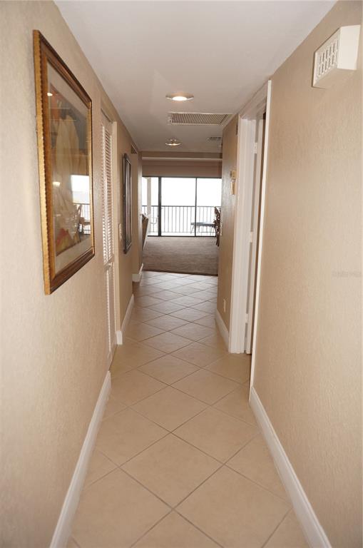 A hallway with tan tile flooring leads to a living area with a balcony view — 1601 PARK BEACH CIRCLE UNIT 125/11, PUNTA GORDA, FL