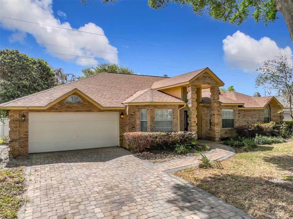 A single-story brick house with a two-car garage and a paved driveway under a blue sky — 9144 GALLEON COURT, ORLANDO, FL