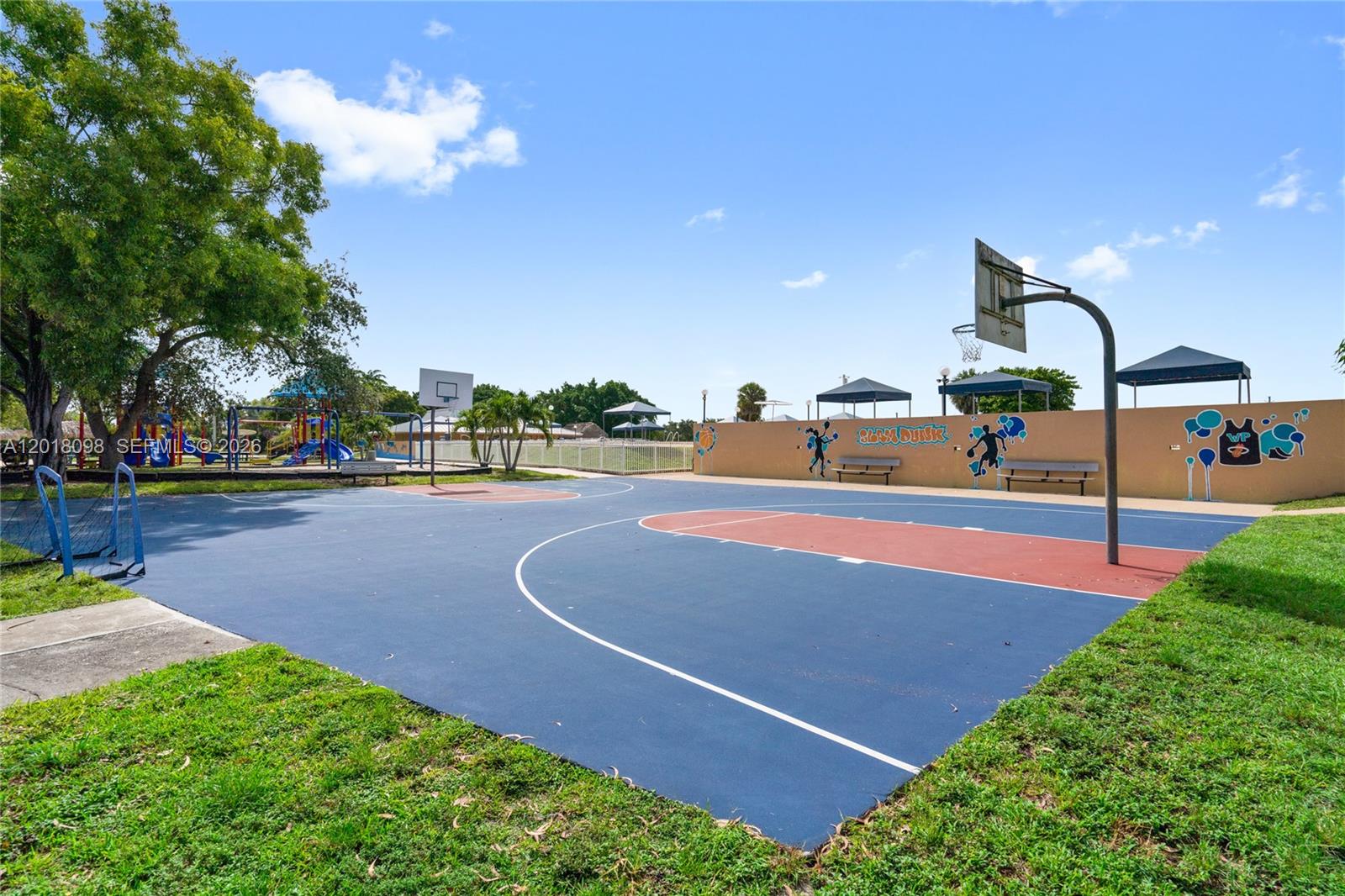 An outdoor basketball court features a blue and red surface with two hoops and benches — 13611 SW 77th St, Miami FL 33183, MIAMI, FL