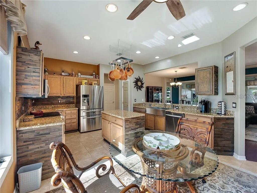 A kitchen features wood-paneled cabinetry, granite countertops, stainless steel appliances, and a glass-topped dining table — 13650 SE 91ST AVENUE, SUMMERFIELD, FL