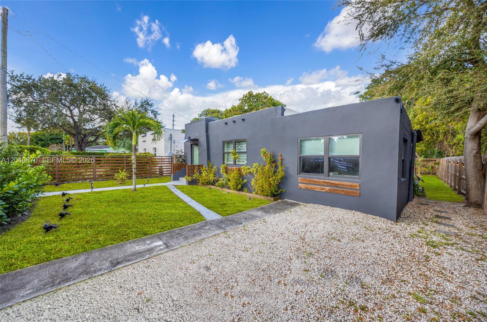 A gray, single-story house features a gravel driveway, a front lawn, and a wooden fence — 5612 NW 11th Ave, Miami FL 33127, MIAMI, FL