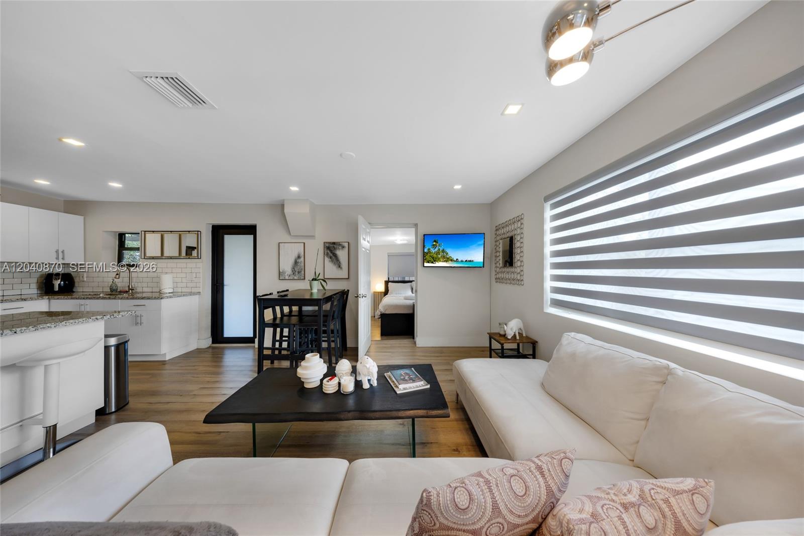 A modern open-concept living room features a white sectional sofa, kitchen, and dining area — 5612 NW 11th Ave, Miami FL 33127, MIAMI, FL