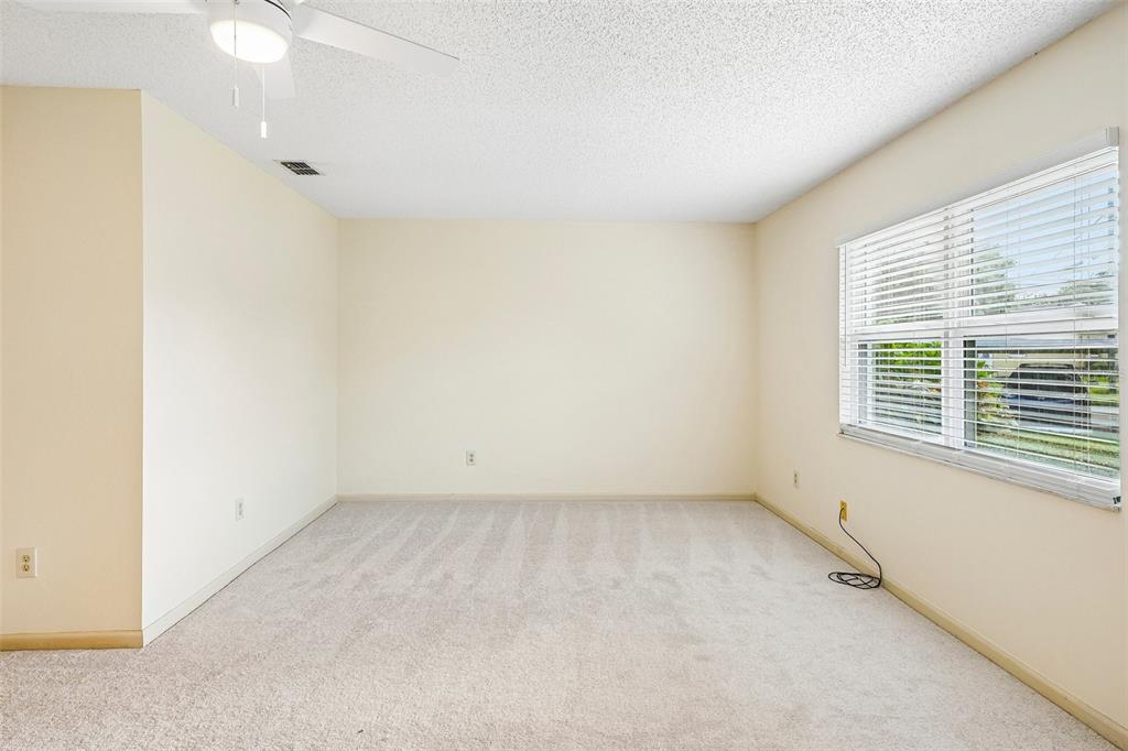 An empty bedroom with beige walls, light-colored carpeting, a ceiling fan, and a large window — 1902 DANDRIDGE STREET UNIT 29, SUN CITY CENTER, FL