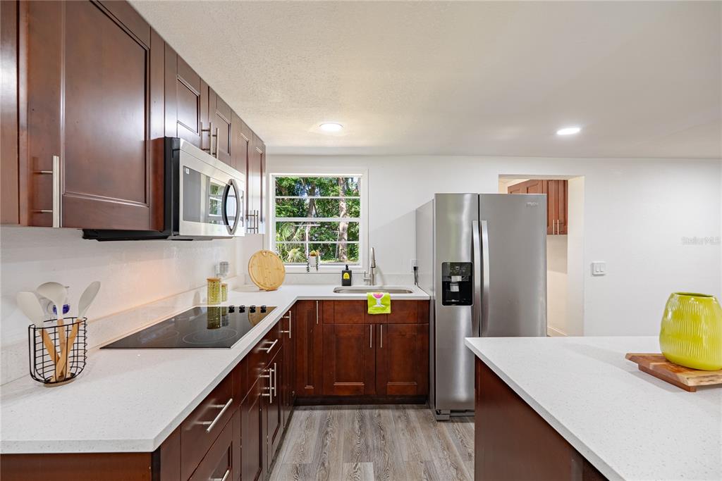 A kitchen features dark wood cabinets, white countertops, stainless steel appliances, and a window — 11303 CHICAGO AVENUE, NEW PORT RICHEY, FL