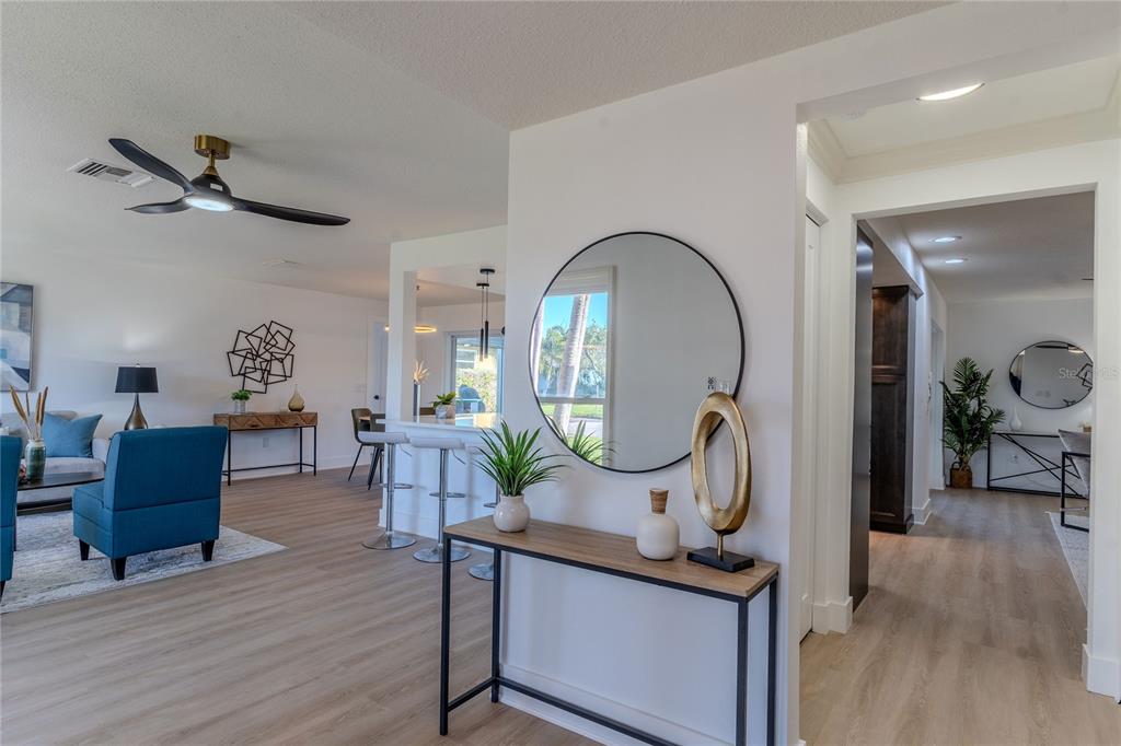 A bright living area features light wood-look flooring, a round wall mirror, and a console table — 3807 48TH AVENUE S, ST PETERSBURG, FL