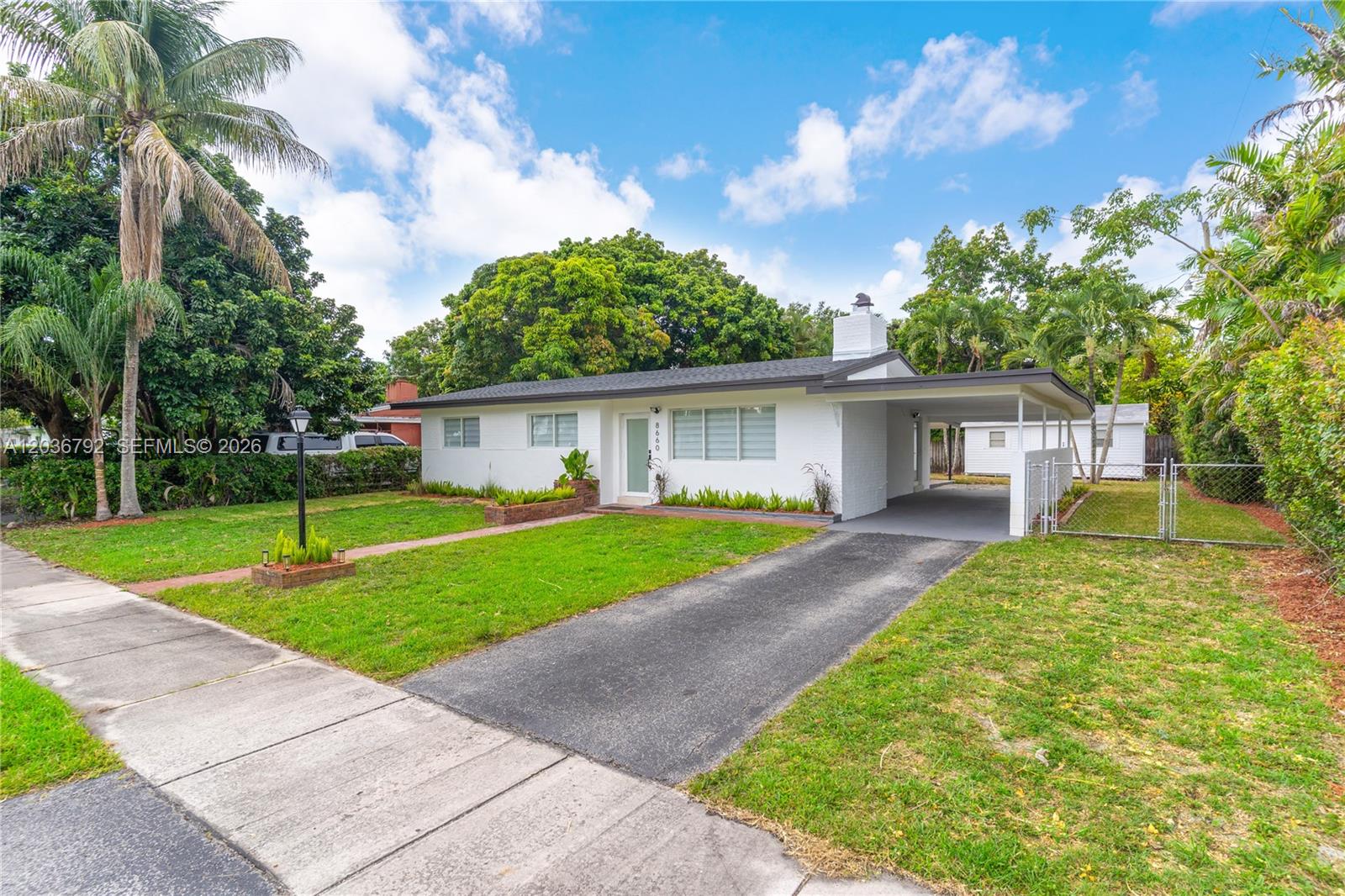 A white single-story house features a carport, a front lawn, and a paved driveway — 8660 SW 125th Ter, Miami FL 33156, MIAMI, FL