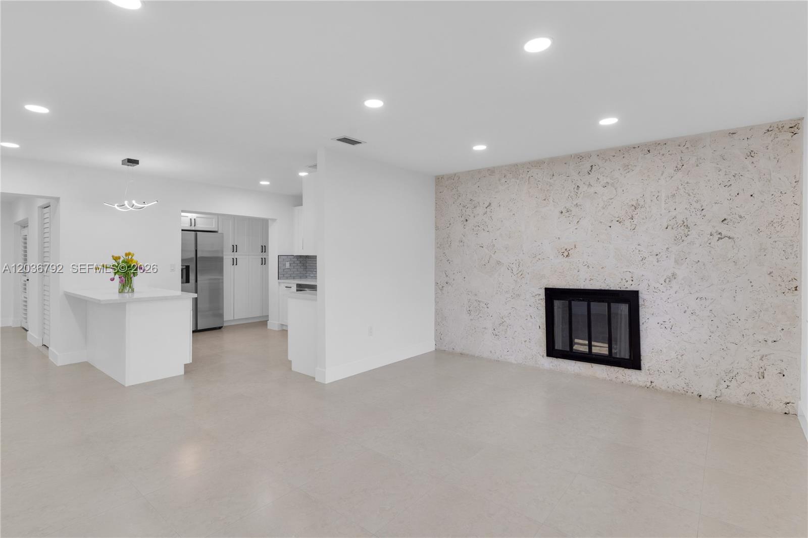 A bright, open-concept living area features a stone fireplace wall and an adjacent white kitchen — 8660 SW 125th Ter, Miami FL 33156, MIAMI, FL