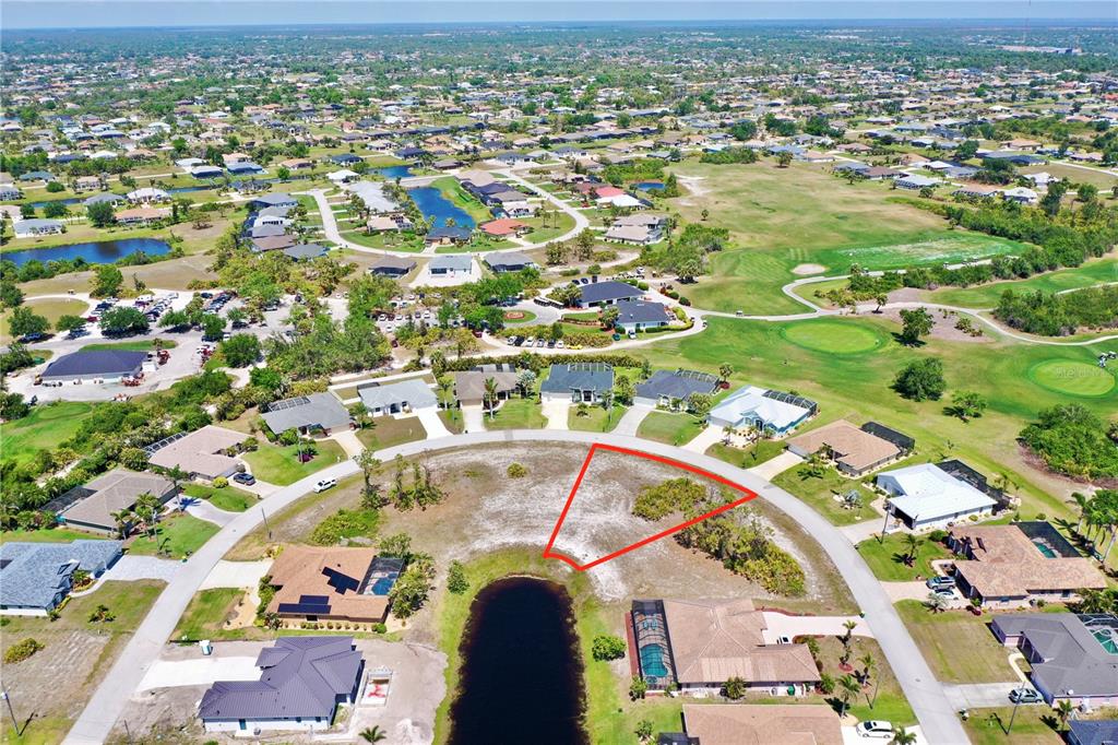 An aerial view shows a vacant, triangular-shaped residential lot situated along a curved street and pond — 13 MEDALIST WAY, ROTONDA WEST, FL