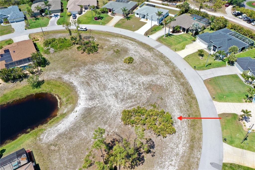 An aerial view shows a vacant, sandy residential lot bordered by a curved road and pond — 13 MEDALIST WAY, ROTONDA WEST, FL